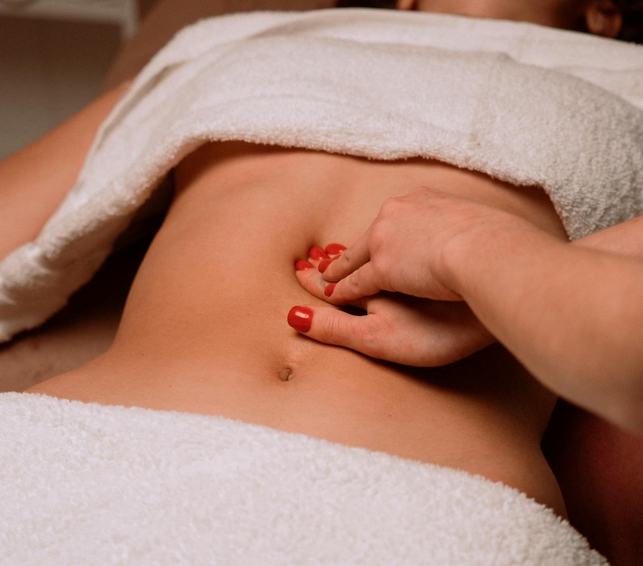Home A soothing massage on a woman's abdomen with painted nails, creating a serene spa atmosphere.